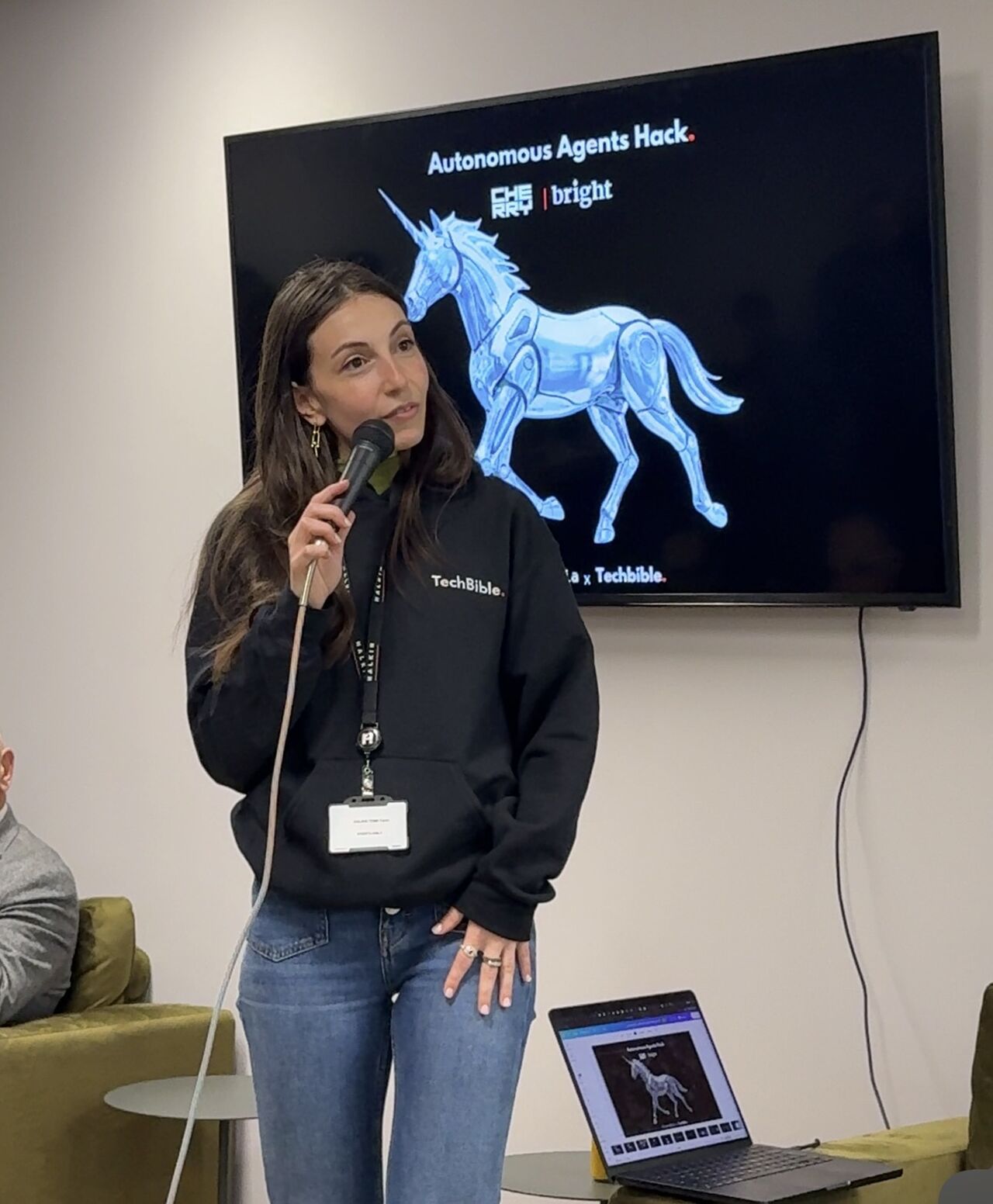 Ghita holding a microphone in front of a screen reading Autonomous Agents Hack with the Cherry and Bright Data logos and a blue wireframe unicorn.