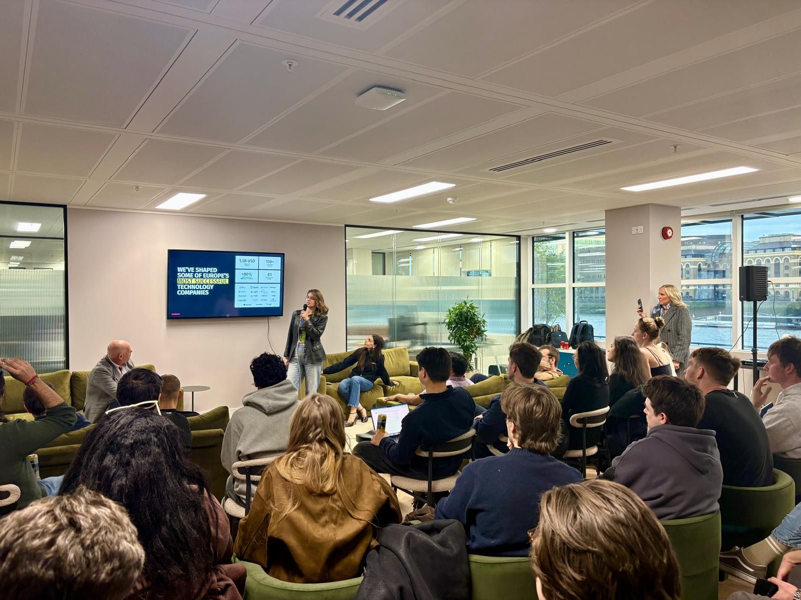 A room of attendees on green velvet seating watching a presenter, with a Thames view and a Cherry Ventures slide on screen.