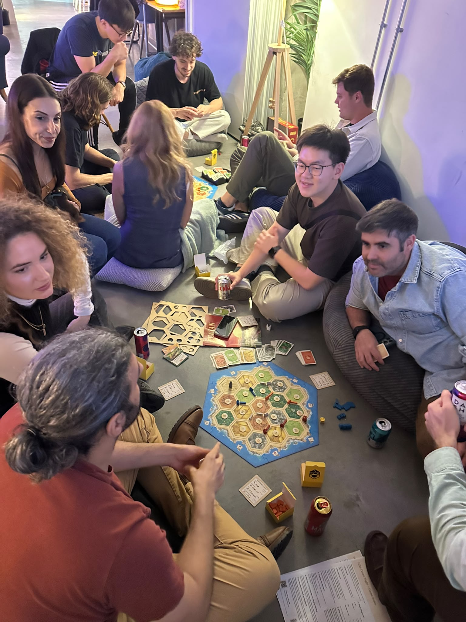 A group of founders and operators sitting on floor cushions around a Catan board, with cards, game pieces and drinks spread across the floor.